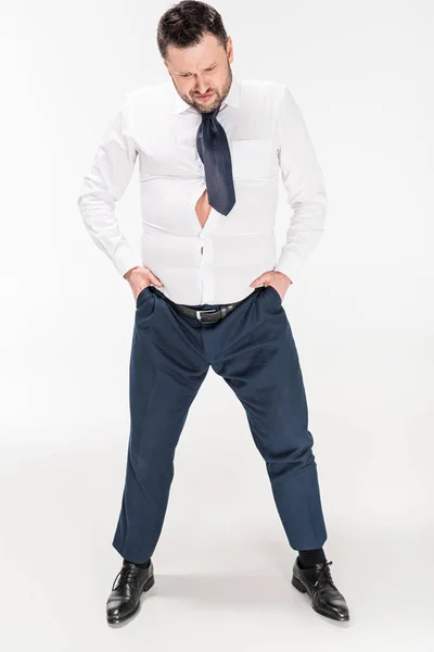 Homme en surpoids en tenue formelle serrée avec les mains dans les poches posant sur blanc — Photo de stock