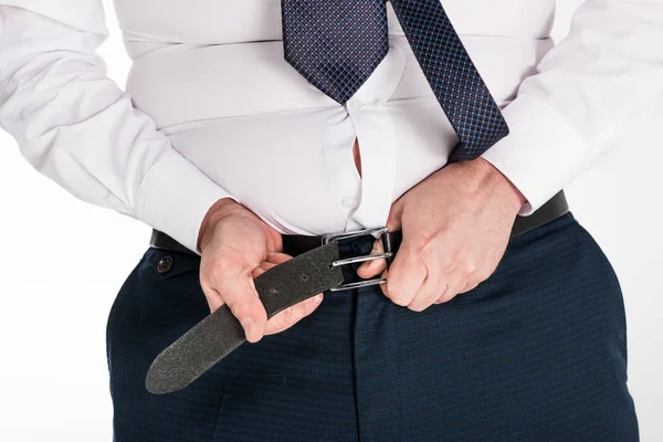 Vista parcial del hombre con sobrepeso en ropa formal poniéndose pantalones ajustados aislados en blanco - foto de stock