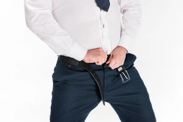 Vista recortada del hombre con sobrepeso en ropa formal poniéndose pantalones ajustados aislados en blanco - foto de stock