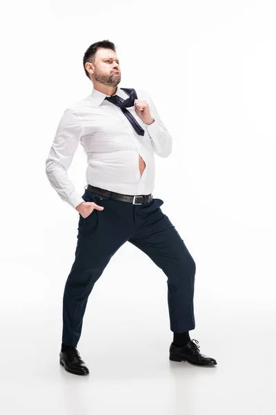 Hombre con sobrepeso en apretado desgaste formal con la mano en el bolsillo posando en blanco - foto de stock