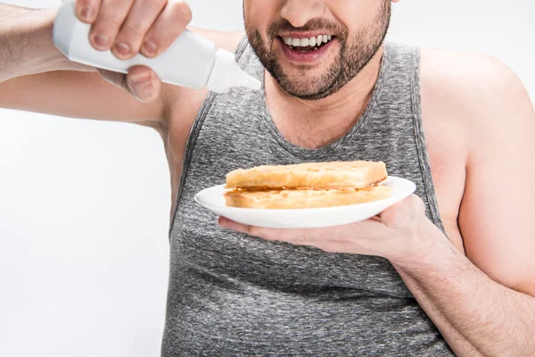 Обрезанный вид человека с избыточным весом, держащего бутылку сиропа и вафли изолированные на белом — стоковое фото
