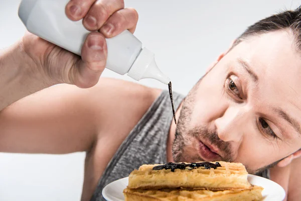 Close up view of chubby man pouring chocolate syrup on waffles isolated on white — Stock Photo