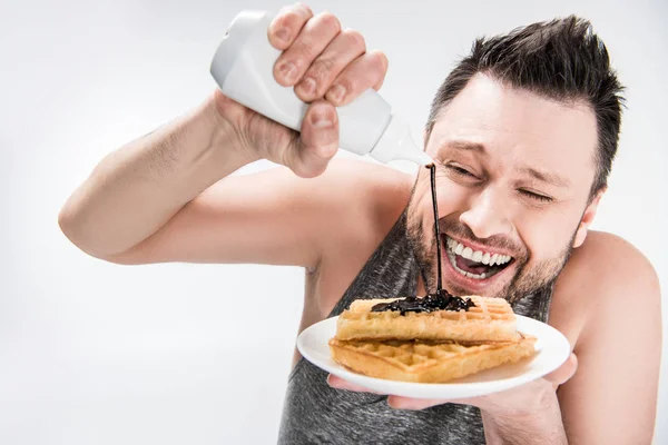 Happy chubby man pouring chocolate syrup on waffles on white — Stock Photo