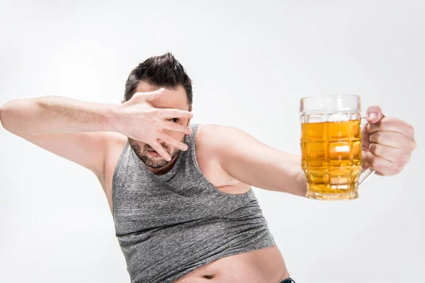 Uomo in sovrappeso che copre il viso con mano e che tiene il bicchiere di birra isolato su bianco — Foto stock