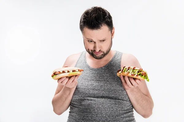 Homme en surpoids dans le débardeur tenant des hot-dogs isolés sur blanc — Photo de stock