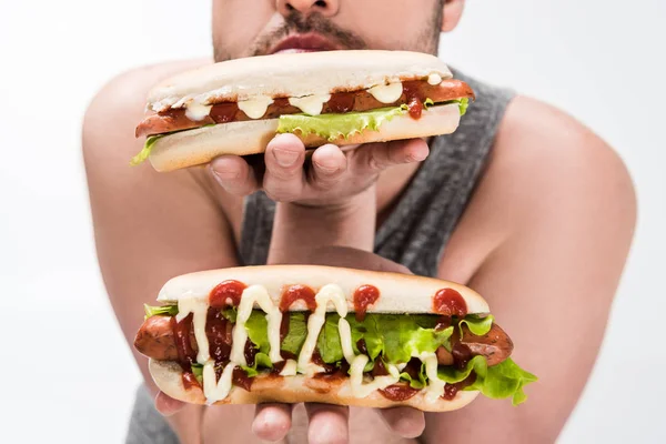 Vista cortada de homem com sobrepeso segurando deliciosos cachorros-quentes isolados em branco — Fotografia de Stock