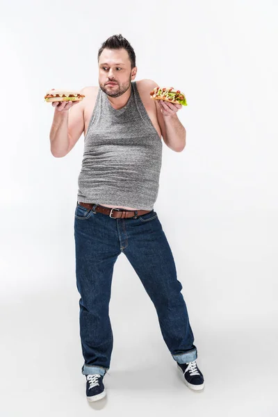 Homme en surpoids dans le débardeur tenant des hot-dogs sur blanc — Photo de stock