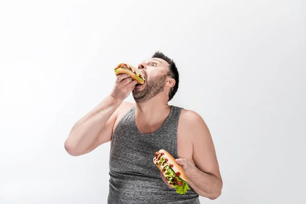 Hungry overweight man in tank top eating hot dog on white — Stock Photo