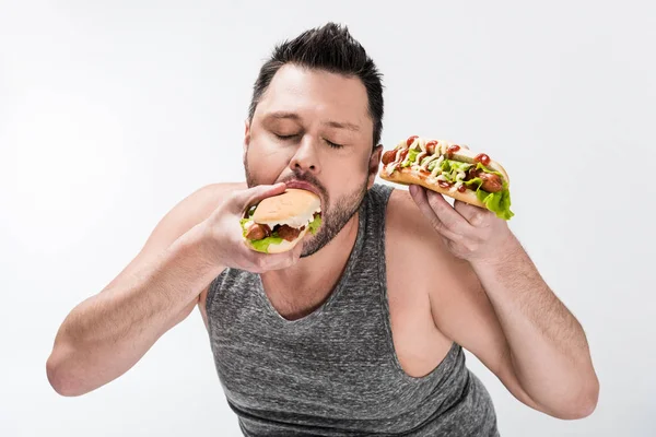 Overweight man in tank top eating tasty hot dog isolated on white — Stock Photo