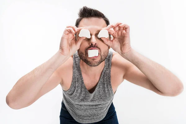 Chubby man in grey tank top holding marshmallows in front of face isolated on white — Stock Photo