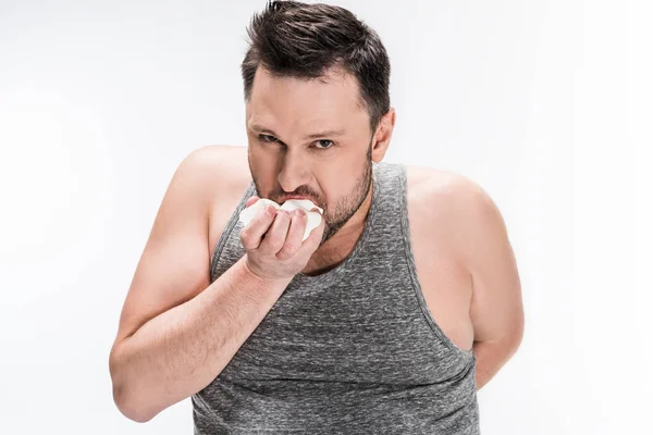 Пухлый человек ест зефир и смотрит на камеру, изолированную на белом — стоковое фото