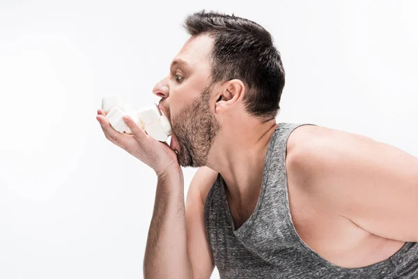 Vista lateral del hombre regordete comiendo malvaviscos aislados en blanco - foto de stock