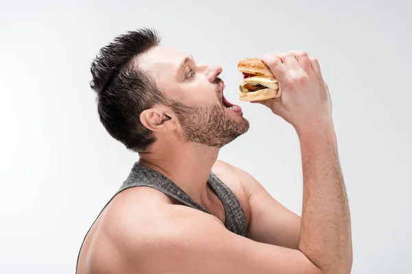 Vista lateral de gordito barbudo hombre comer hamburguesa aislado en blanco - foto de stock