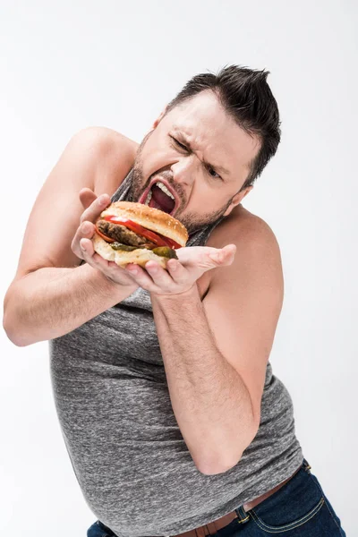 Übergewichtiger Mann macht Gesichtsausdruck, während er mit Burger isoliert auf Weiß posiert — Stockfoto