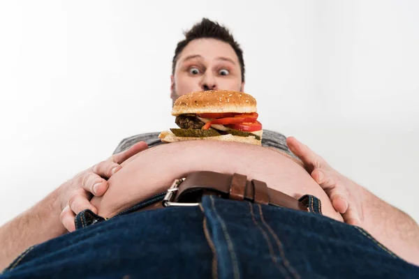 Shocked overweight man with burger on belly isolated on white — Stock Photo