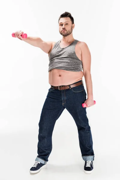 Homem com sobrepeso olhando para a câmera enquanto trabalhava com halteres rosa no branco — Fotografia de Stock