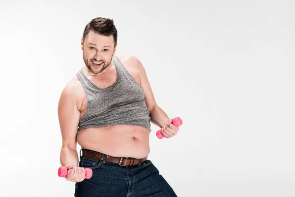 Glücklicher übergewichtiger Mann, der in die Kamera schaut, während er mit rosafarbenen Hanteln trainiert, isoliert auf weiß mit Kopierraum — Stockfoto