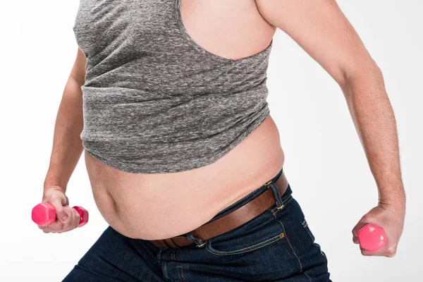 Vista parcial del hombre con sobrepeso mostrando el vientre y haciendo ejercicio con pesas rosadas aisladas en blanco - foto de stock