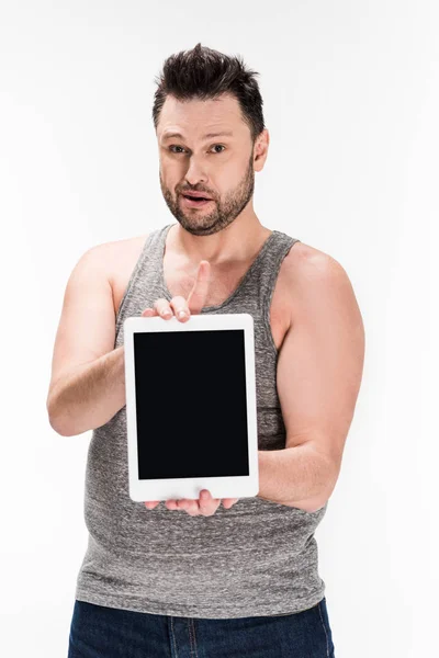 Человек с избыточным весом смотрит в камеру и показывает цифровой планшет с чистым экраном, изолированным на белом — стоковое фото