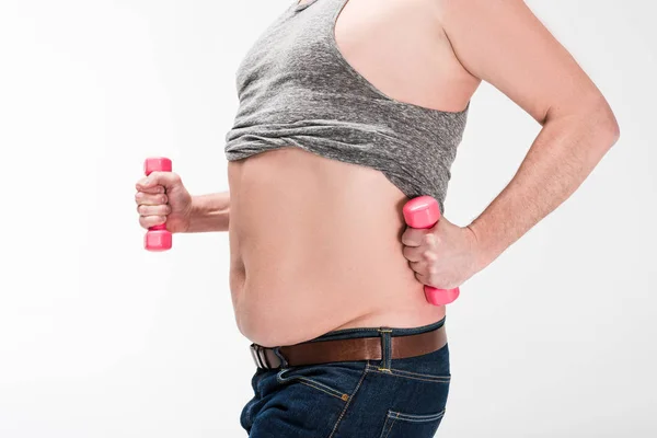 Vue recadrée de l'homme en surpoids montrant le ventre et l'exercice avec des haltères roses isolés sur blanc — Photo de stock