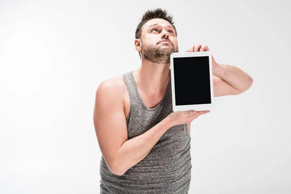 Übergewichtiger Mann schaut auf und zeigt digitales Tablet mit leerem Bildschirm isoliert auf weißem Hintergrund — Stockfoto