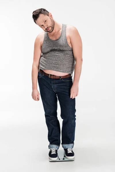 Sovrappeso uomo guardando la fotocamera mentre in piedi su bilance elettroniche di peso isolato su bianco — Foto stock