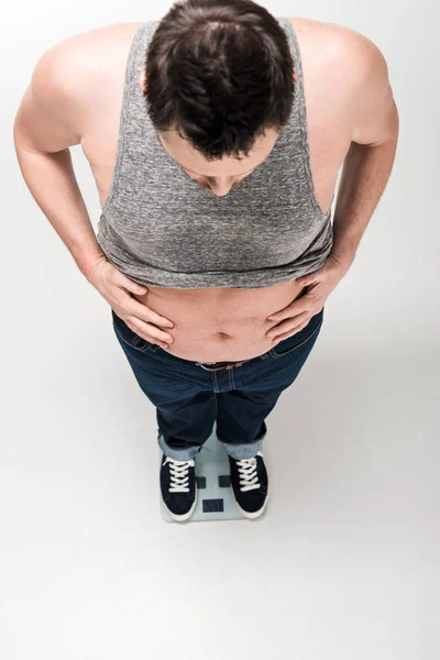 High angle view of overweight man holding belly while standing on electronic weight scales isolated on white — Stock Photo