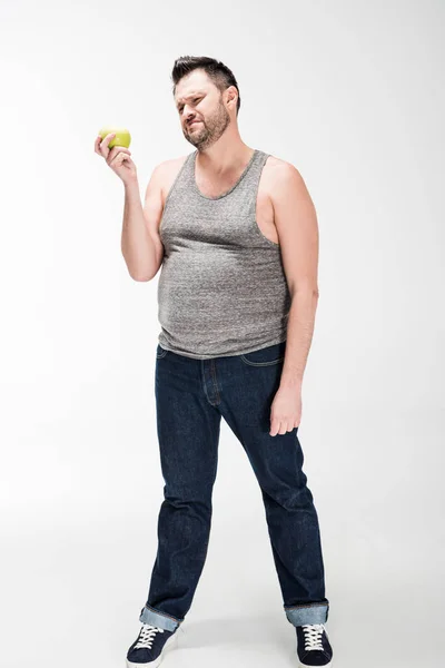 Dissatisfied overweight man in tank top holding green apple on white — Stock Photo