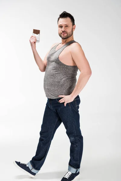 Homme en surpoids regardant la caméra et posant avec du chocolat sur blanc — Photo de stock