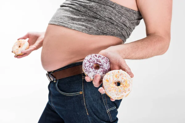 Abgeschnittene Ansicht eines übergewichtigen Mannes, der Bauch zeigt und Donuts isoliert auf Weiß hält — Stockfoto