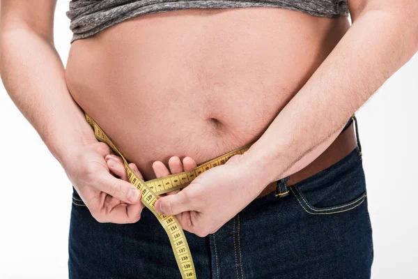 Cropped view of overweight man measuring waistline with tape isolated on white — Stock Photo