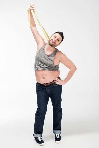 Homem com sobrepeso colando a língua para fora e segurando fita métrica no branco — Fotografia de Stock
