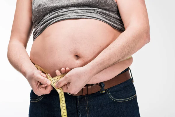 Cropped view of overweight man measuring waistline with tape isolated on white — Stock Photo