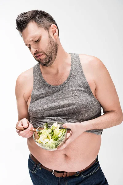 Displeased overweight man holding bowl of salad on white — Stock Photo