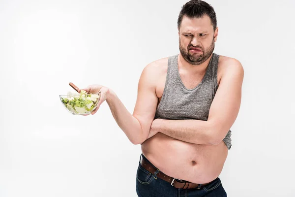 Hombre con sobrepeso sosteniendo tazón de ensalada en disgusto aislado en blanco - foto de stock