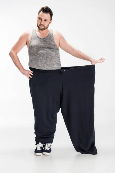 Homem com sobrepeso segurando calças grandes após a perda de peso e olhando para a câmera no branco — Fotografia de Stock