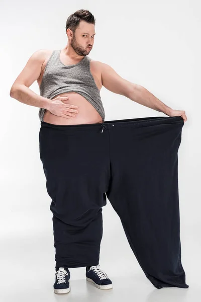 Sovrappeso uomo toccando pancia mentre tenendo pantaloni oversize dopo la perdita di peso su bianco — Foto stock