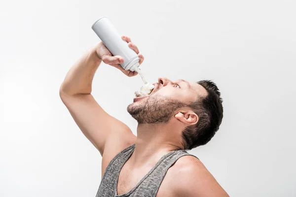 Molliger Mann im Tanktop sprüht Schlagsahne in den Mund auf weiß — Stockfoto