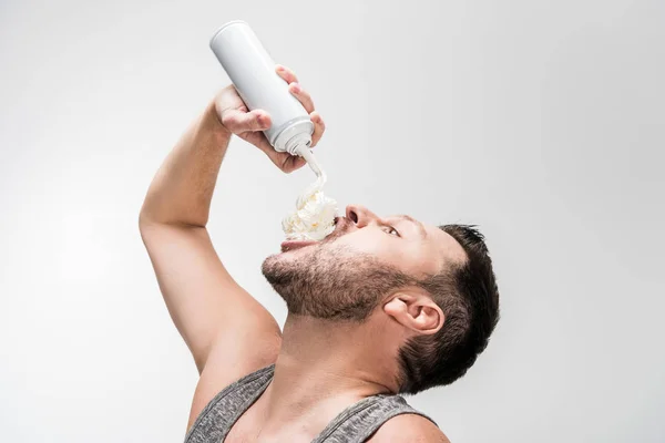 Gordito hombre rociando crema batida en la boca en blanco - foto de stock