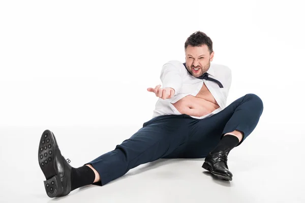 Angry overweight man in tight formal wear gesturing with hand while sitting on white — Stock Photo