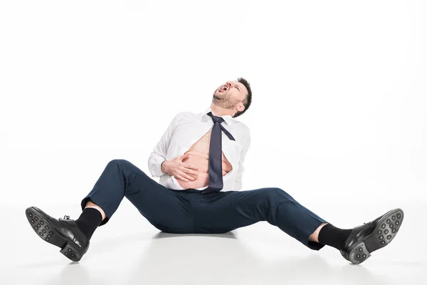 Angry overweight man in tight formal wear touching belly while sitting on white — Stock Photo