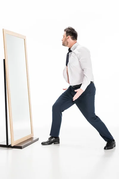 Overweight man in formal wear gesturing while looking at mirror on white — Stock Photo