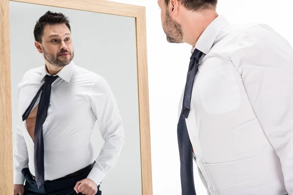 Надмірна вага людини в офіційному одязі, дивлячись на відображення в дзеркалі ізольовано на білому — стокове фото