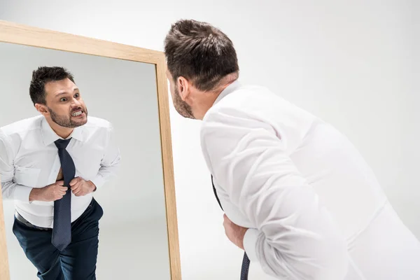 Homme en surpoids en colère dans l'usure formelle en regardant la réflexion dans le miroir sur blanc — Photo de stock