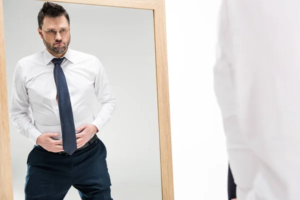 Insatisfait homme joufflu en tenue formelle regardant miroir isolé sur blanc avec espace de copie — Photo de stock