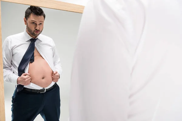 Übergewichtiger Mann in formeller Kleidung, der auf Spiegel mit Kopierraum schaut, isoliert auf Weiß — Stockfoto