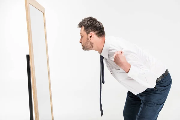 Hombre con sobrepeso en desgaste formal inclinándose y mirando el espejo aislado en blanco - foto de stock