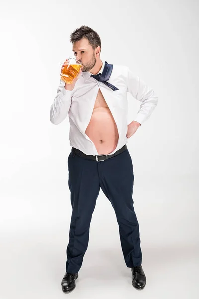 Overweight man in tight shirt drinking glass of beer on white — Stock Photo