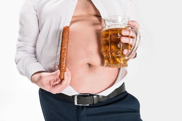 Частичный вид человека с избыточным весом, показывающего живот и стакан пива с жареной колбасой, изолированной на белом — стоковое фото