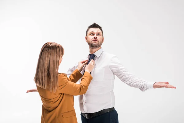 Mujer en traje ajustando corbata de hombre con sobrepeso gesto con las manos aisladas en blanco - foto de stock